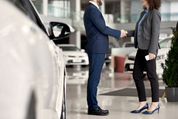 Two people shaking hands in a car dealership.