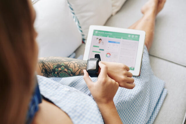 Woman looking at her watch with tablet sitting on her lap