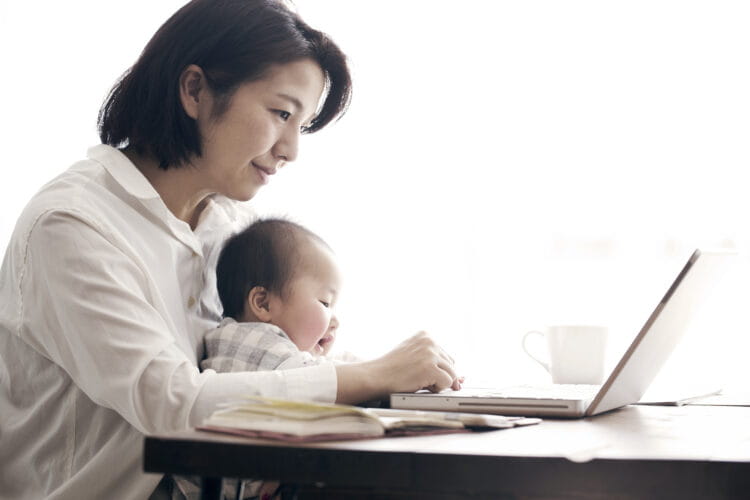 A woman working on a laptop with her baby on her lap.