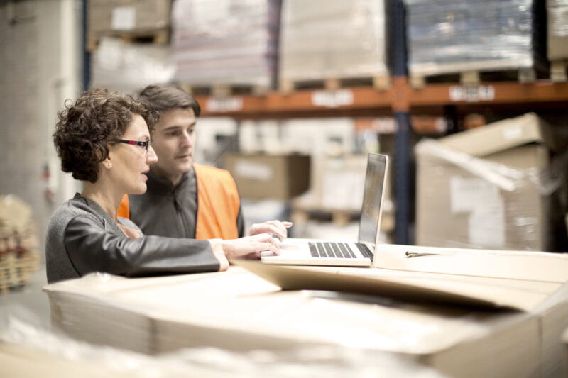 Two people working on a computer in a warehouse.