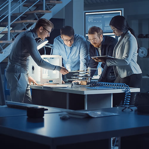 A group of people in a lab standing around a table working on something 