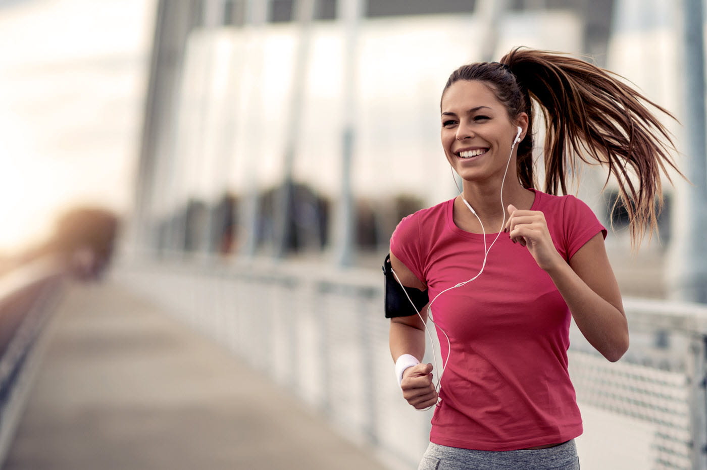 A woman with headphones in running and smiling.