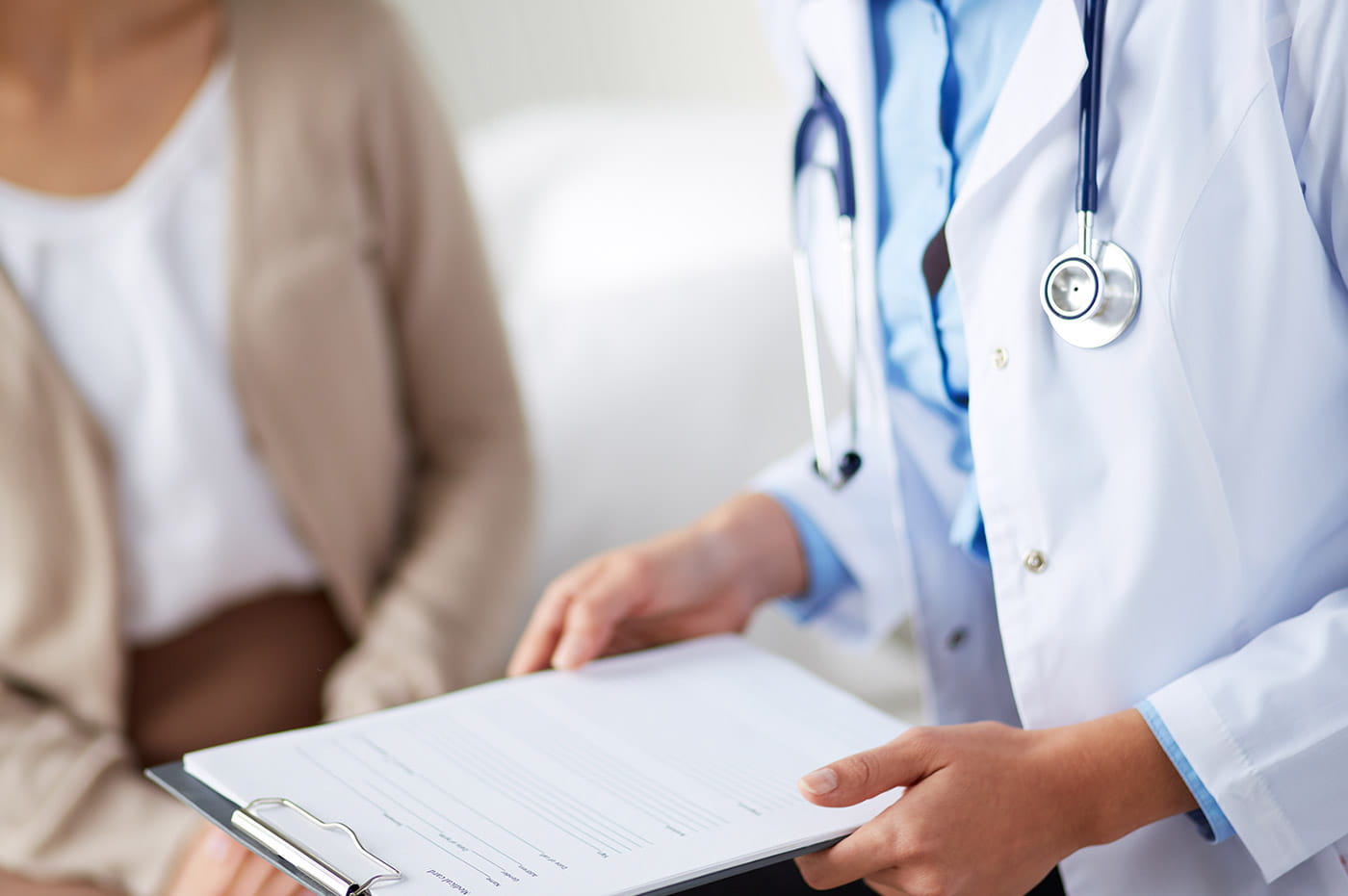 Man in lab coat holding some documents on a clipboard and standing next to a patient.