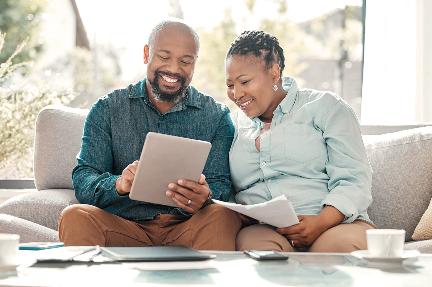 Smiling couple sitting on a couch with an iPad and papers. 