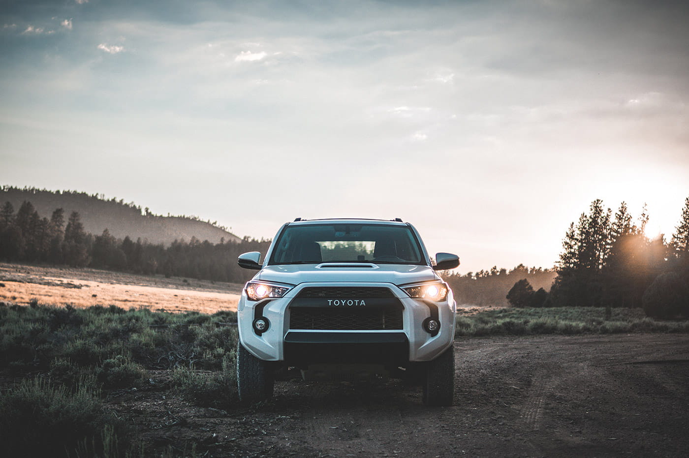 A Toyota vehicle with its headlights on in an area with trees and dirt.