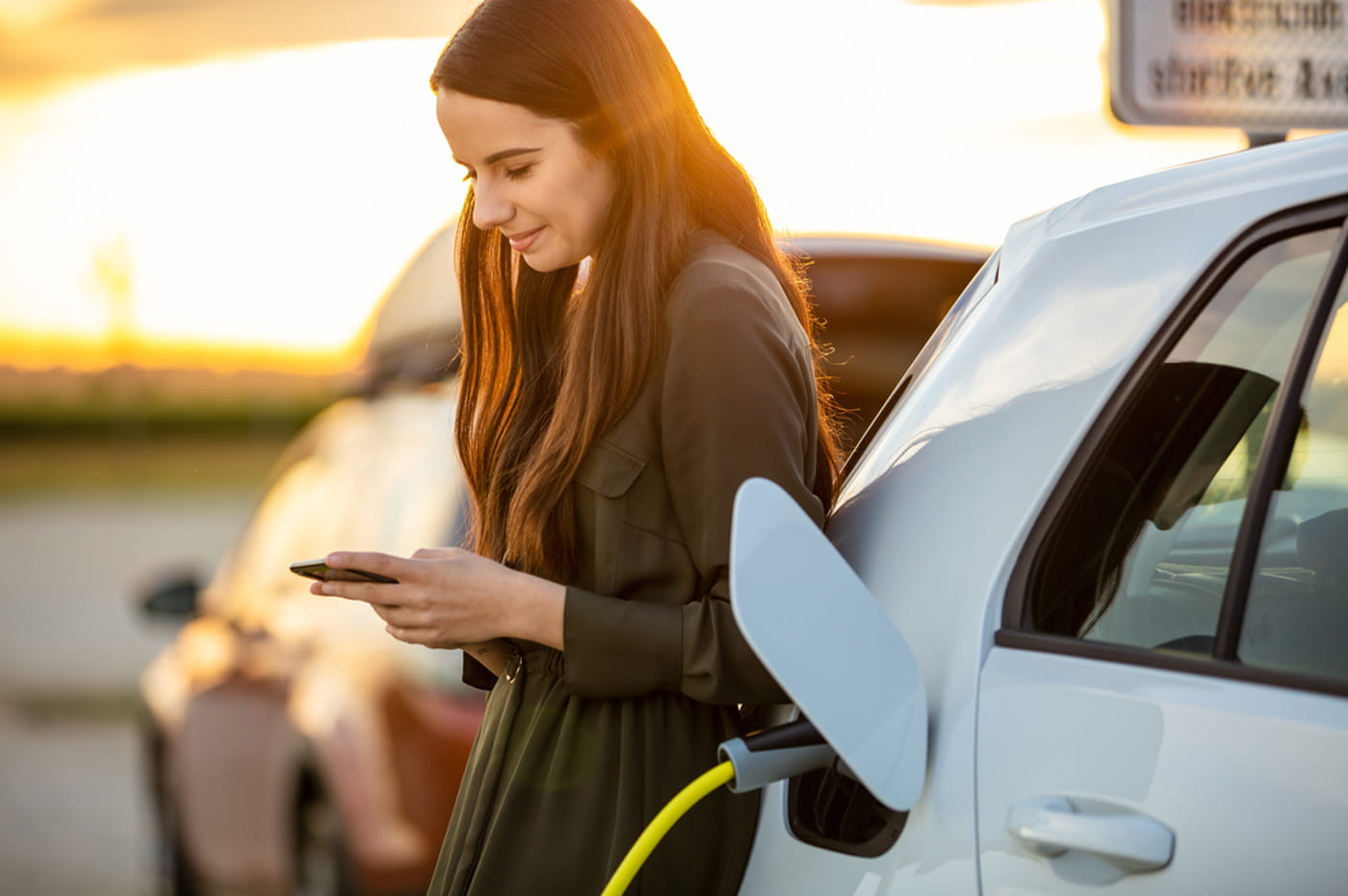 Woman on phone waiting for electric car to charge