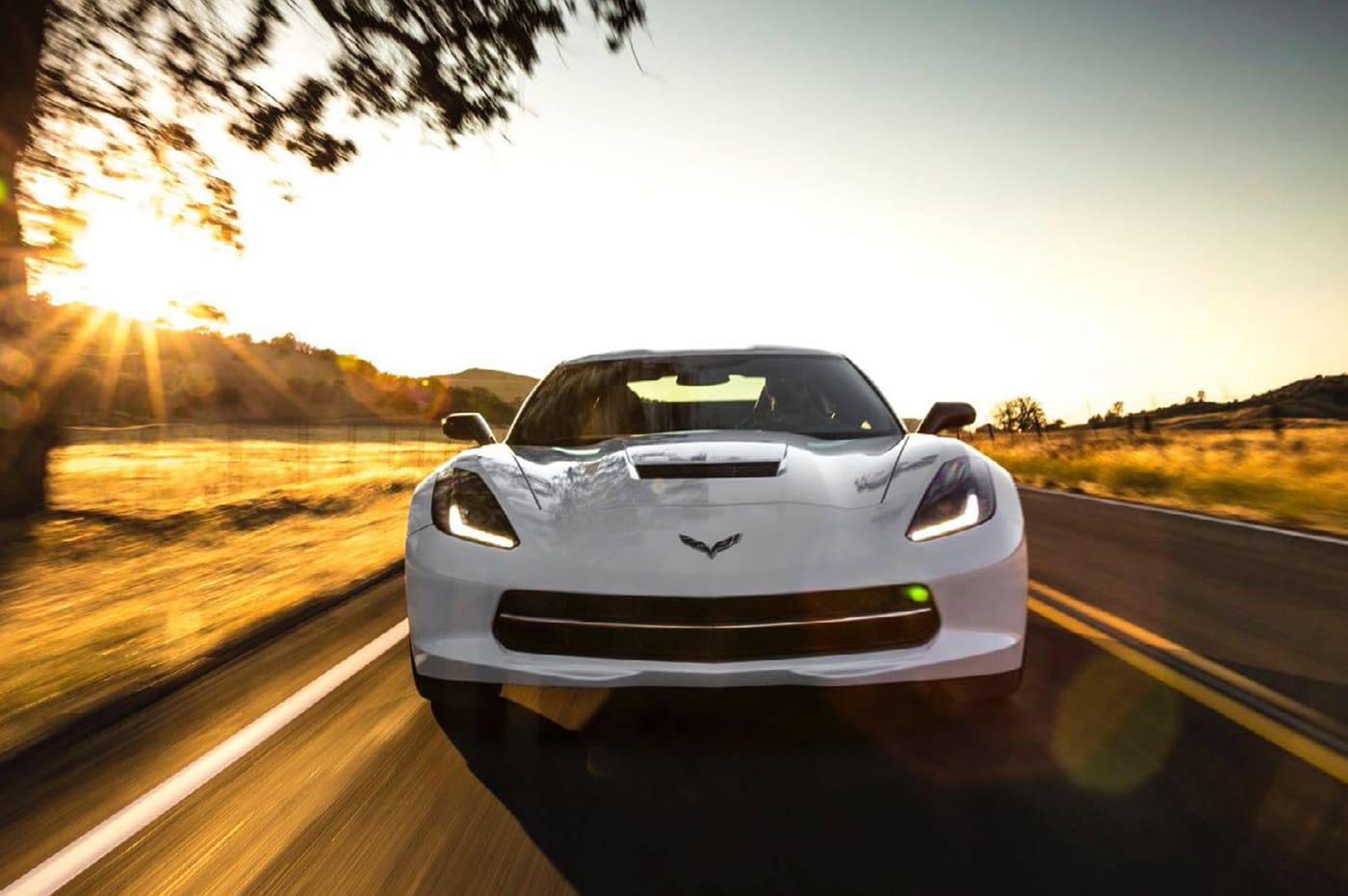 A white corvette driving down a road.