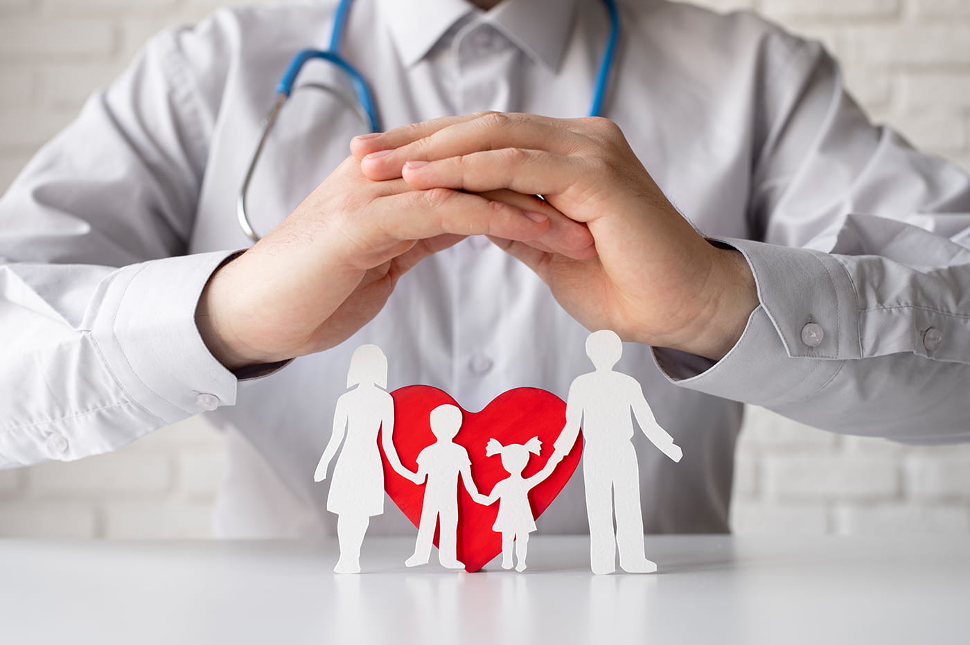 Doctor holding hands over paper family with heart in the background