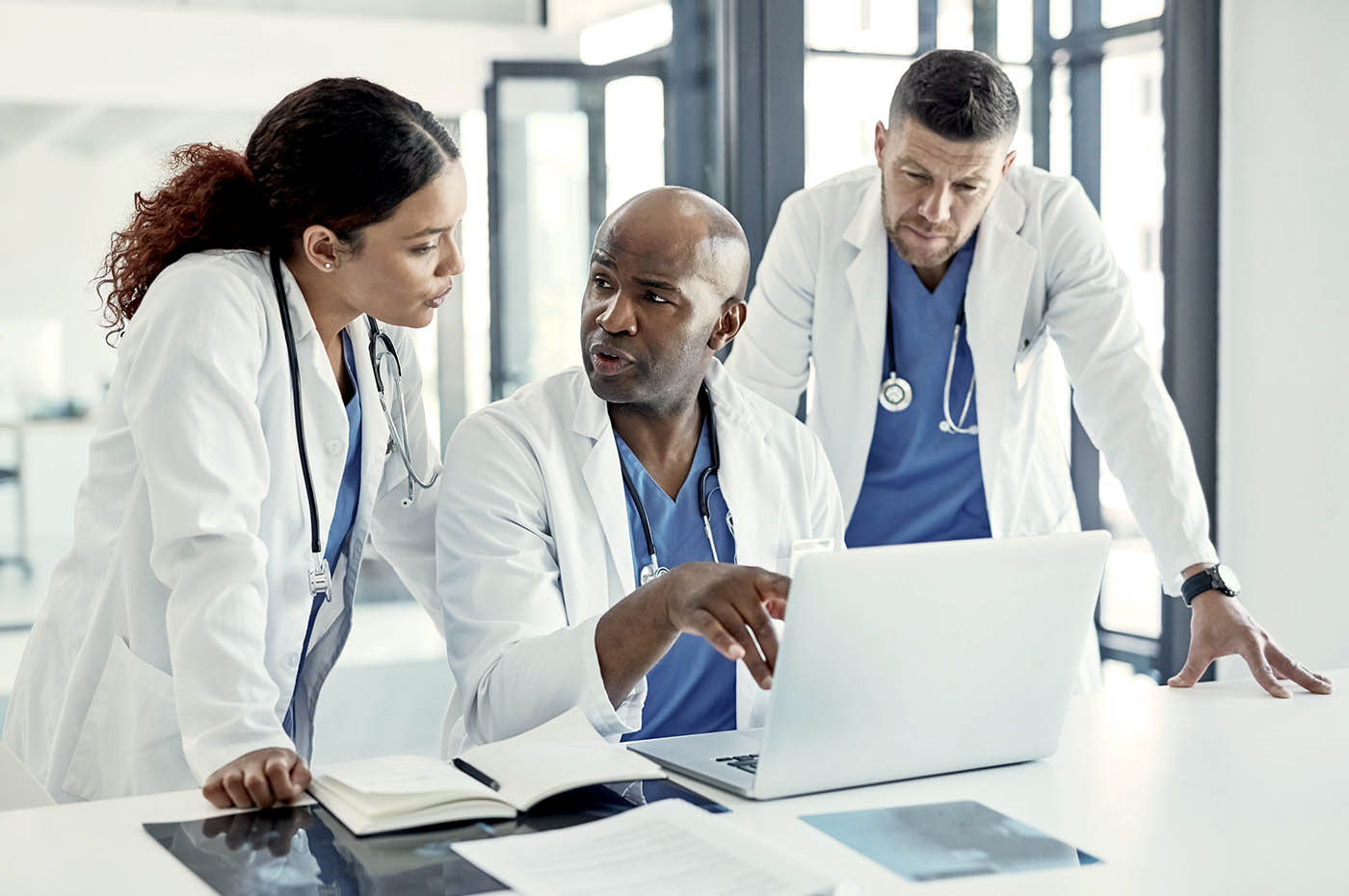 Three doctors gathered around a laptop computer and talking.