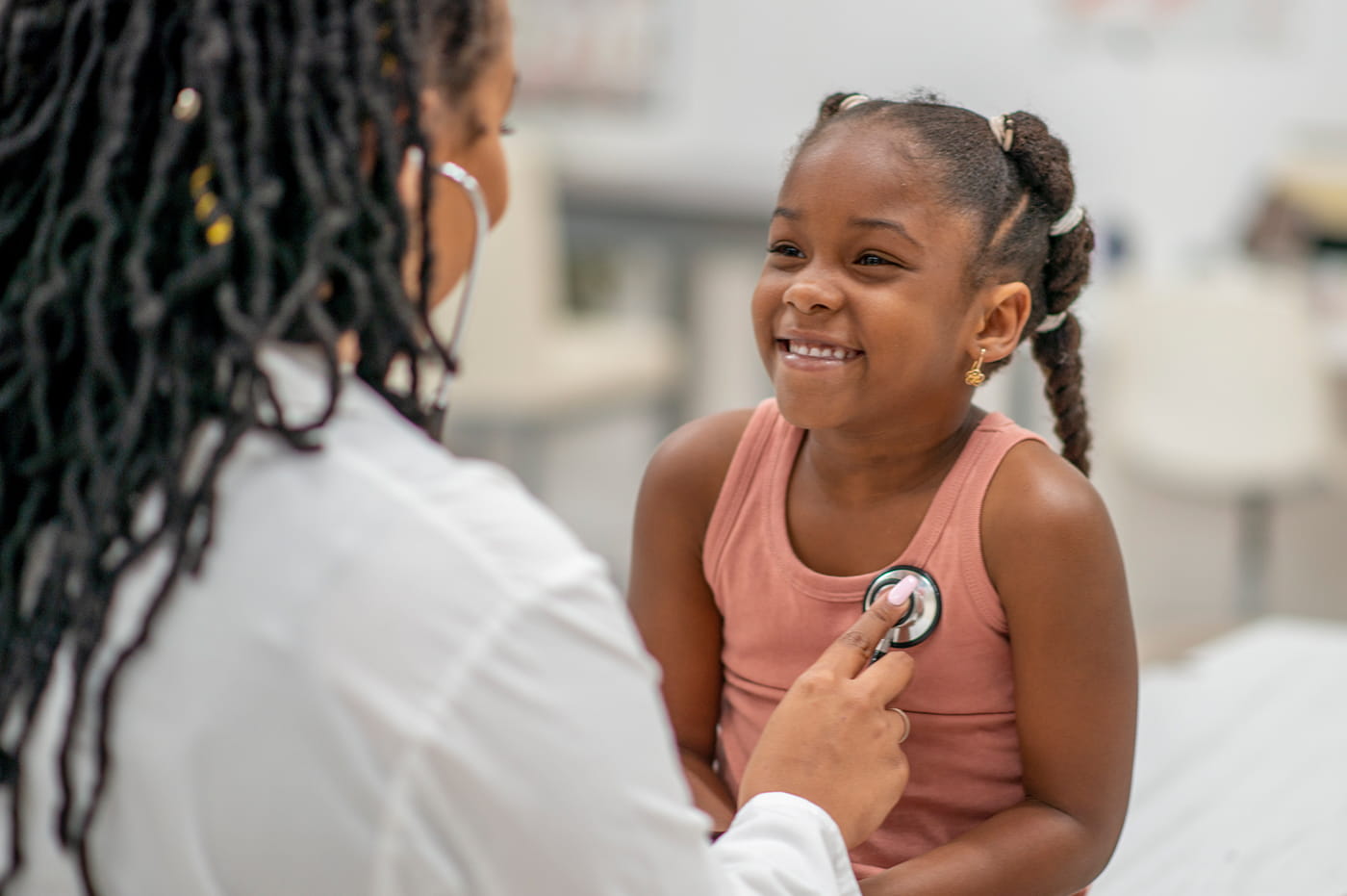 A doctor using a stethoscope to listen to a little girl's heart.